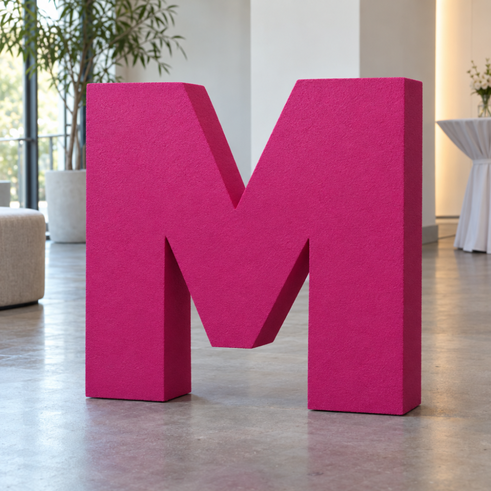 Stor M i mattlakkert polystyren med sokkel, vist på gulvet i et arrangementsområde