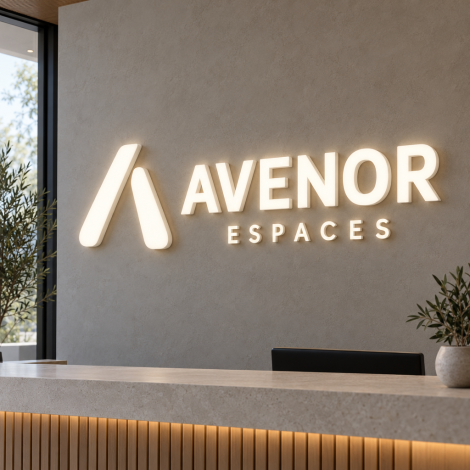 Oplyst logoskilt i plexiglas med AVENOR og linjen ESPACES, varm hvid finish, monteret på en væg i receptionen.